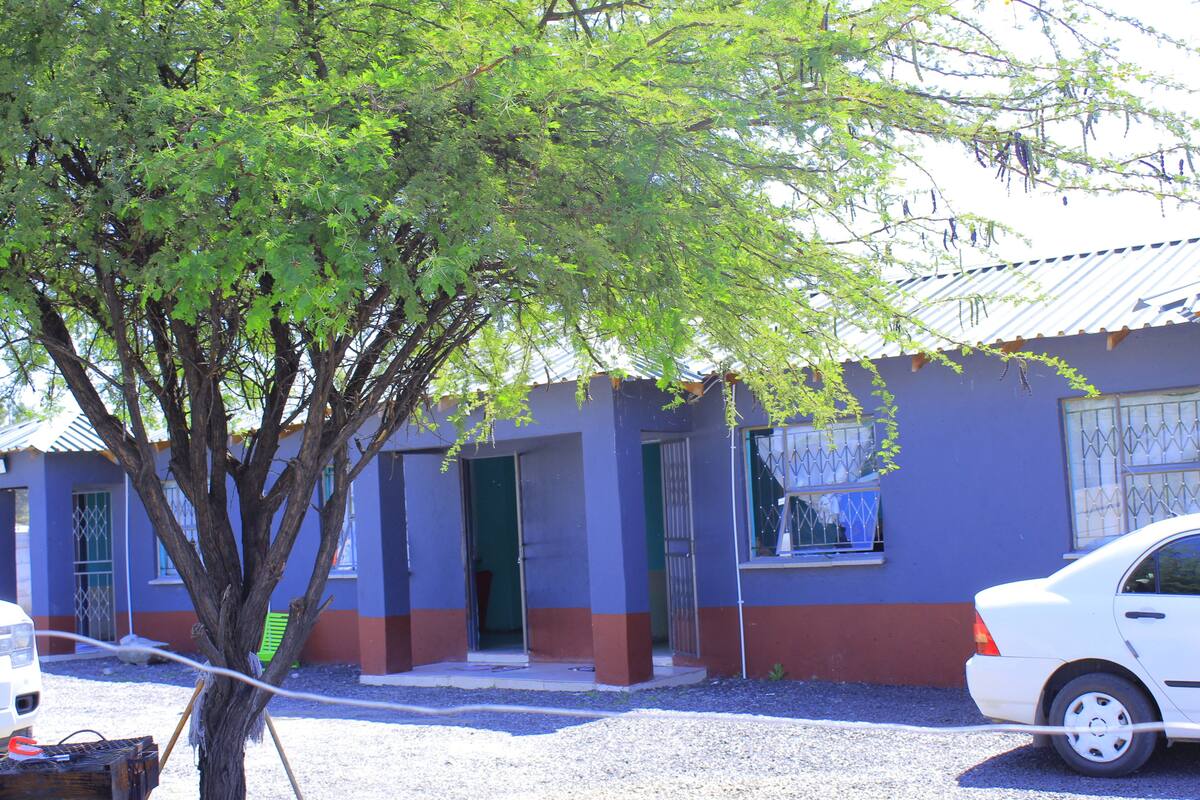 Un edificio con un árbol frente a él, un coche estacionado cerca y una ventana con una reja de metal.