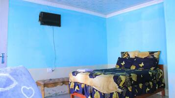 Una habitación con cama, un banco, un televisor de pared y una colcha estampada.