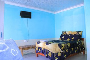 A room with a bed, a bench, a wall-mounted television, and a patterned bedspread.