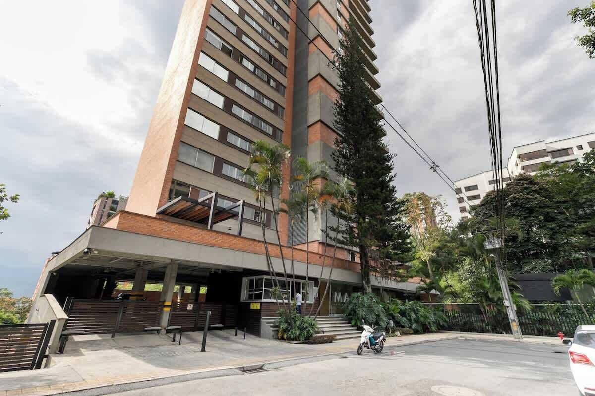 Un edificio de varios pisos con un acceso cubierto, mesas al aire libre y un estacionamiento.