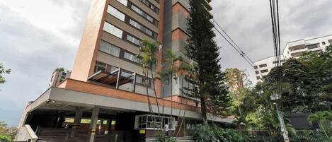 Un edificio de varios pisos con un acceso cubierto, mesas al aire libre y un estacionamiento.