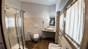A bathroom with a stone wall, a glass shower enclosure, a sink, and a toilet. - Aristonsuite (Piazza Armerina)