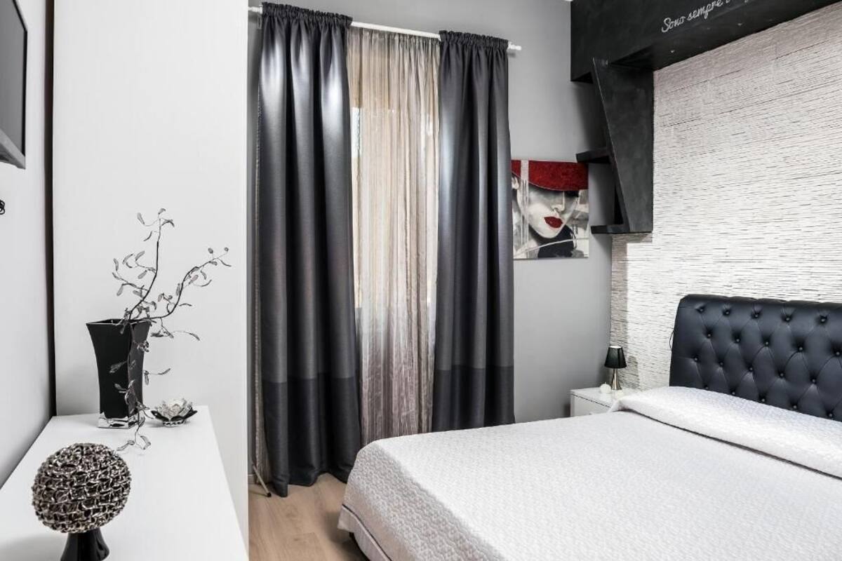 Un dormitorio moderno con una cama, una mesita de noche, una lámpara, un florero con una planta y un cuadro en la pared.