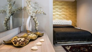A modern bedroom with a tufted headboard, a decorative wall panel, and a bedside table with a vase of flowers. - Aristonsuite (Piazza Armerina)