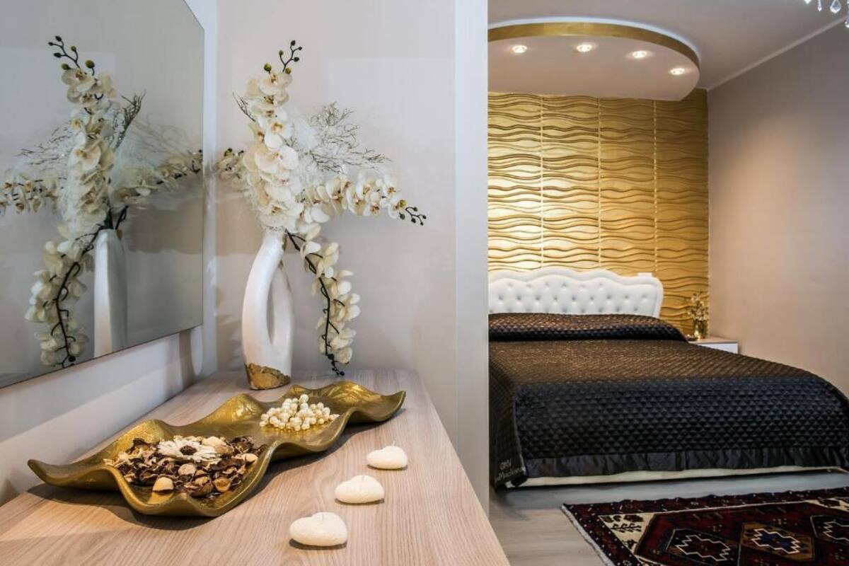 Un dormitorio moderno con cabecera capitonada, un panel decorativo en la pared y una mesita de noche con un jarrón de flores.