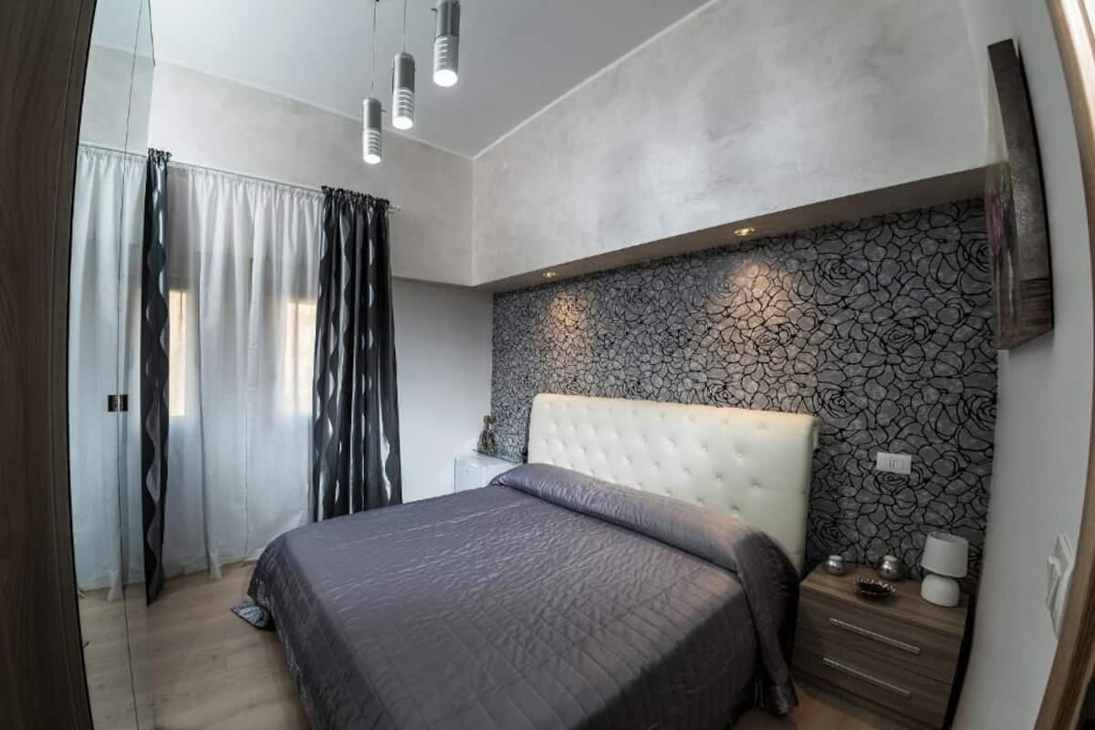 Un dormitorio con una cama, mesitas de noche, un espejo y un papel tapiz estampado.