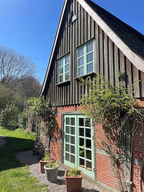 A traditional wooden house with a steep gable roof, a brick foundation, and a green door. - Auszeit vom Alltag: Ferienhaus zwischen Ostsee & Schlei - 4 Personen (Rieseby)