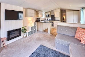 A modern living room with a flat-screen TV, a fireplace, a grey sofa, and a kitchen area with cabinets and appliances. - Host Stay Cedar Lodge (York)