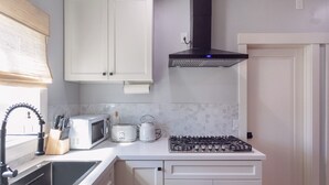 A compact kitchen with white cabinets, a microwave, a kettle, and a gas stove. - 2BR Cozy Home Serene Garden Retreat Near UC Berkeley San Francisco (Richmond)