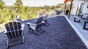 An outdoor seating area with Adirondack chairs and a grill, overlooking a forested landscape. - The Overlook on Mountain View (Lead)