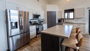 A modern kitchen with stainless steel appliances, a central island, and a dining area. - The Overlook on Mountain View (Lead)