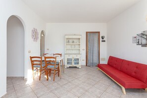 A dining area with a white cabinet, a red sofa, and a tiled floor.