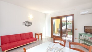 A room with a red sofa, a dining table with chairs, a small wooden side table, a wall-mounted light fixture, and a sliding glass door leading to an outdoor area. - Holiday Home 'San Teodoro House with Garden' with Mountain View, Wi-Fi and Air Conditioning (Suaredda-traversa)