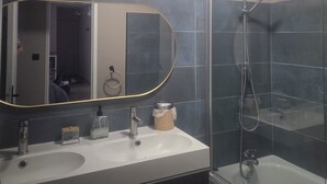 A bathroom with a double sink, a large mirror, a shower enclosure, and a ceiling light.