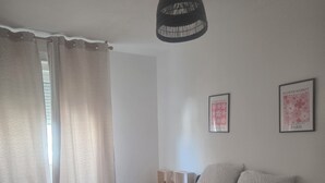 A bedroom with a bed, a hanging light fixture, a window with curtains, and two wall-mounted pictures.