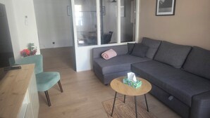 A modern living room with a grey sofa, a small round wooden table, a teal armchair, and a window with a view.