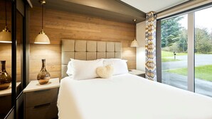 Une chambre d’hôtel moderne avec un grand lit, une tête de lit en bois, des lampes de chevet et une vue sur l’extérieur.