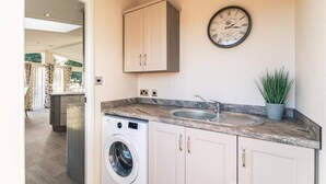 A kitchen with a washing machine, a sink, cabinets, and a clock on the wall. - Host Stay Woodland Jewel Lodge (York)