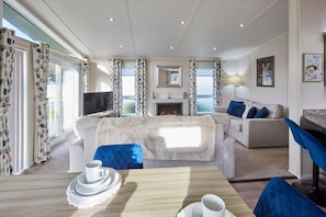 Ein modernes Wohnzimmer mit Kamin, Fernseher und Essbereich mit Tisch für zwei Personen.
