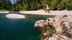 A person jumping off a rocky ledge into a river surrounded by dense forest. - Coastal Cabin Getaway & Animal Sanctuary (Brookings)