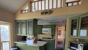A kitchen with a central island, green cabinets, a microwave, and a toaster. - Coastal Cabin Getaway & Animal Sanctuary (Brookings)