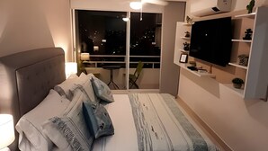 Une chambre moderne avec un lit, une télévision et un balcon offrant une vue nocturne.