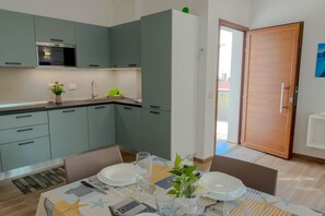 A modern kitchen with grey cabinets, a built-in oven, and a dining area with a table set for two. - Appartamento Lido residence 2 (Cala Gonone)