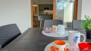Een eetgedeelte met een tafel gedekt voor twee personen, een keuken op de achtergrond en een uitzicht door een glazen deur.