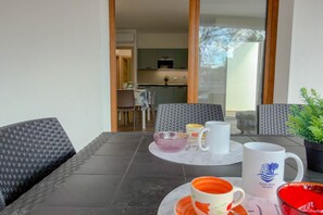 A dining area with a table set for two, a kitchen in the background, and a view through a glass door. - Appartamento Lido residence 2 (Cala Gonone)