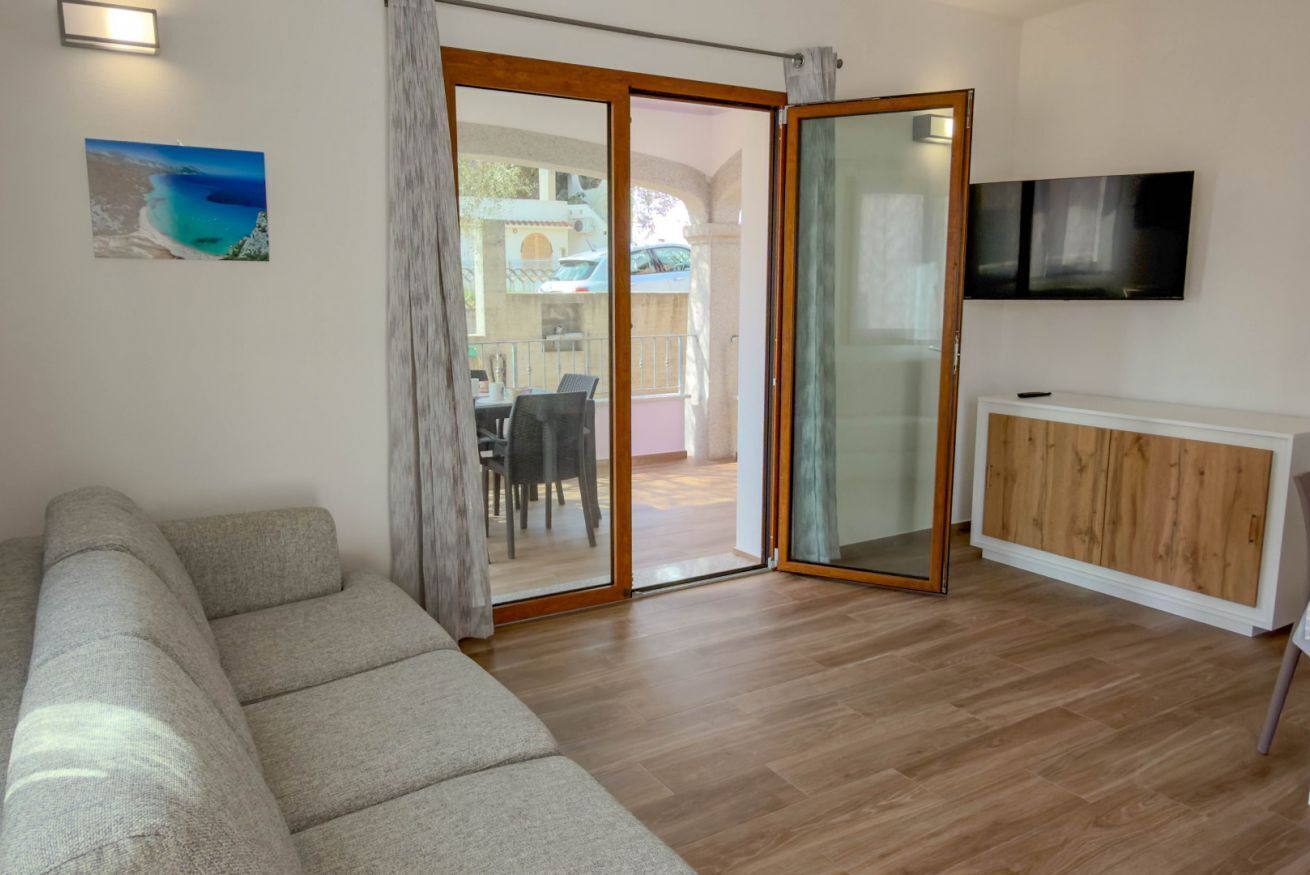 Un soggiorno con un divano, una TV e una porta scorrevole in vetro che dà su un balcone.
