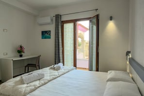 A hotel room with a bed, a desk, a chair, and a view through a glass door. - Appartamento Lido residence 2 (Cala Gonone)