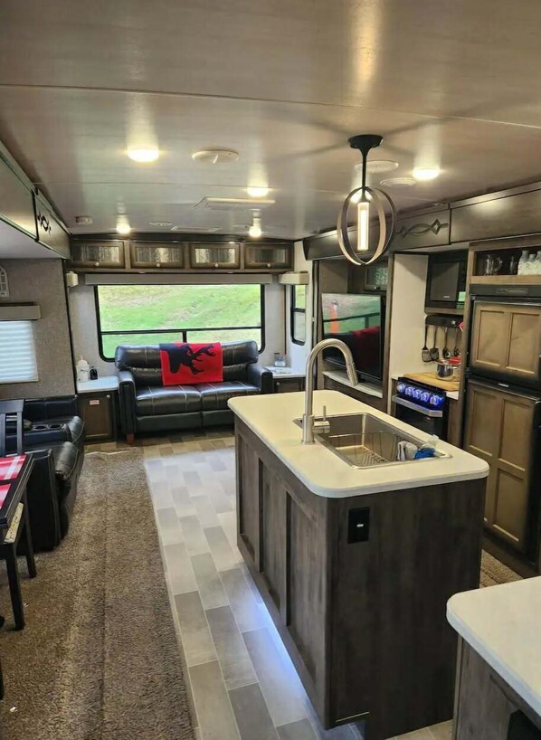 Cocina compacta con una isla central, comedor con sofá y vistas a zonas verdes.