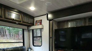 Un salón con un sofá de cuero negro, un televisor de pantalla plana, una chimenea y un ventanal con vistas a un bosque.