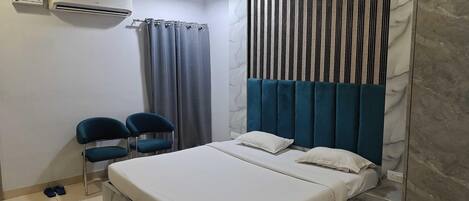 Un dormitorio con cama, dos sillas, un armario, un ventilador de techo y un equipo de aire acondicionado.