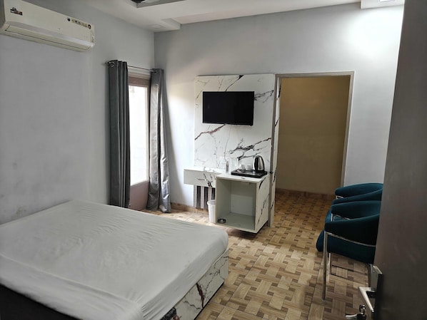 A hotel room with a bed, a desk with a chair, a TV mounted on the wall, and a wardrobe.