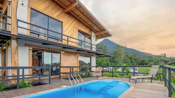 Ein modernes, zweistöckiges Gebäude mit Swimmingpool, Holzterrasse und Blick auf die Berge.