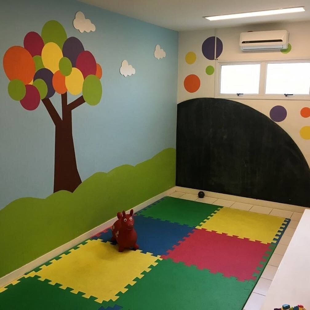 A room with a colorful wall mural, a black curved partition, and a play area with interlocking foam mats.