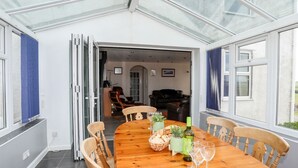 A dining area with a wooden table, chairs, and a glass ceiling. - Bodlasan Groes Cottage (Holyhead)
