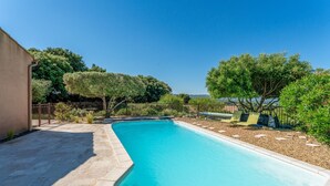 A swimming pool with a curved edge, surrounded by a pebble-lined deck and a fence.