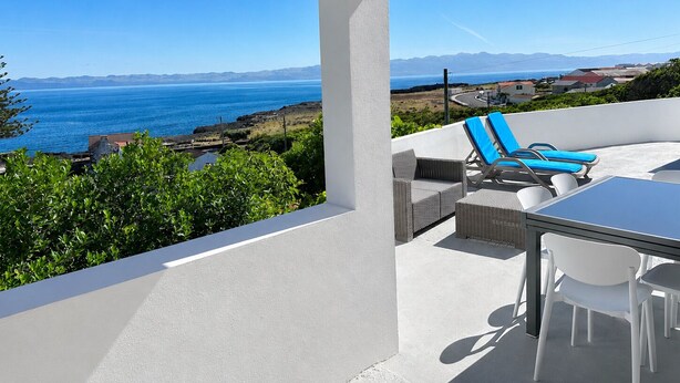 Ein Balkon mit Blick auf das Meer und die Berge, mit Korbmöbeln und einem Tisch.