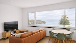 Ein modernes Wohnzimmer mit großem Fenster, einem Flachbildfernseher, einer Ledersofa, einem runden Holztisch mit Stühlen und einem kleinen Beistelltisch.