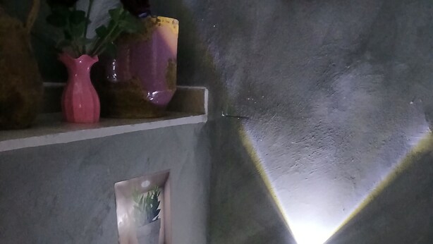 Ein Zimmer mit einer Betonwand, einem kleinen Fenster und einem Regal mit einer Vase und einer Pflanze.