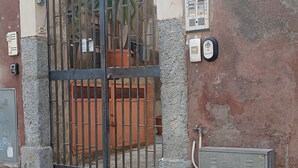 Ein verschlossener Eingang mit einem Metallgitter, einer Treppe, die zu einer Tür führt, und zwei an der Wand befestigte Gehäuse mit der Aufschrift 'Sidr'.