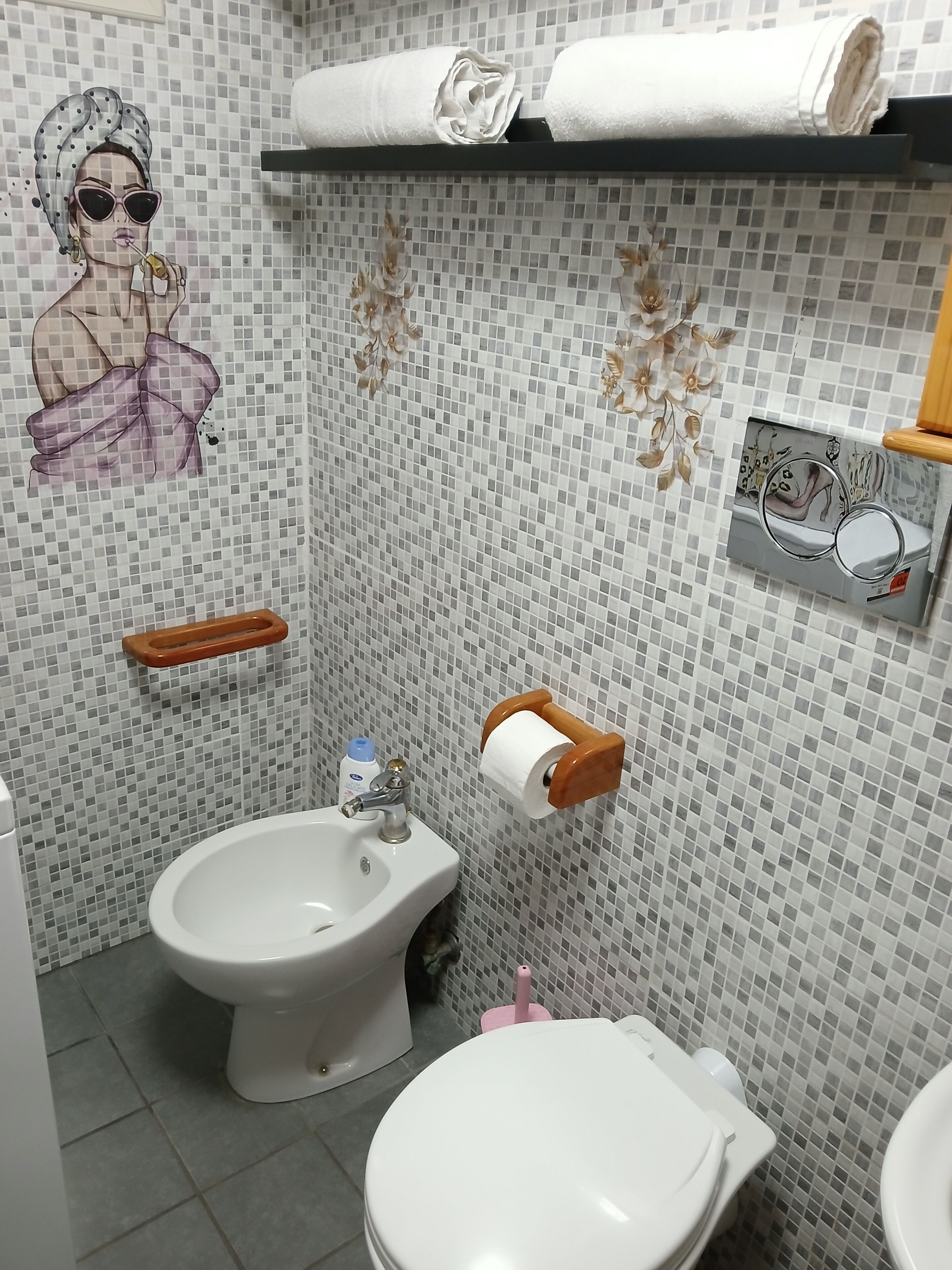 Un baño con bidé, inodoro y un estante con toallas.