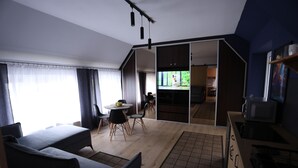 Uma sala de estar moderna com sofá, mesa de jantar e cadeiras, área de cozinha com micro-ondas e uma porta deslizante que dá para outro cômodo.