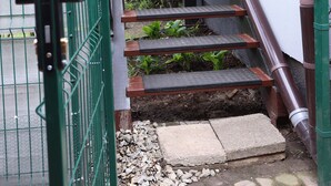 Uma escadaria com grades de metal e um portão verde, que leva a um edifício com fachada branca.