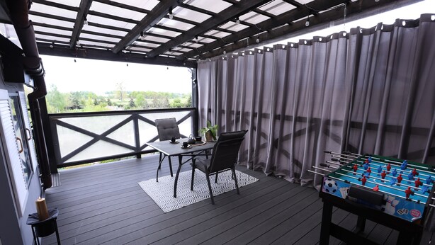 Espaço coberto ao ar livre com mesa de futebol de mesa, uma mesa com cadeiras e vista para o verde.