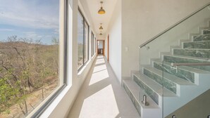 Un interior moderno con una escalera de cristal, ventanas amplias y un pasillo que conduce a una puerta.