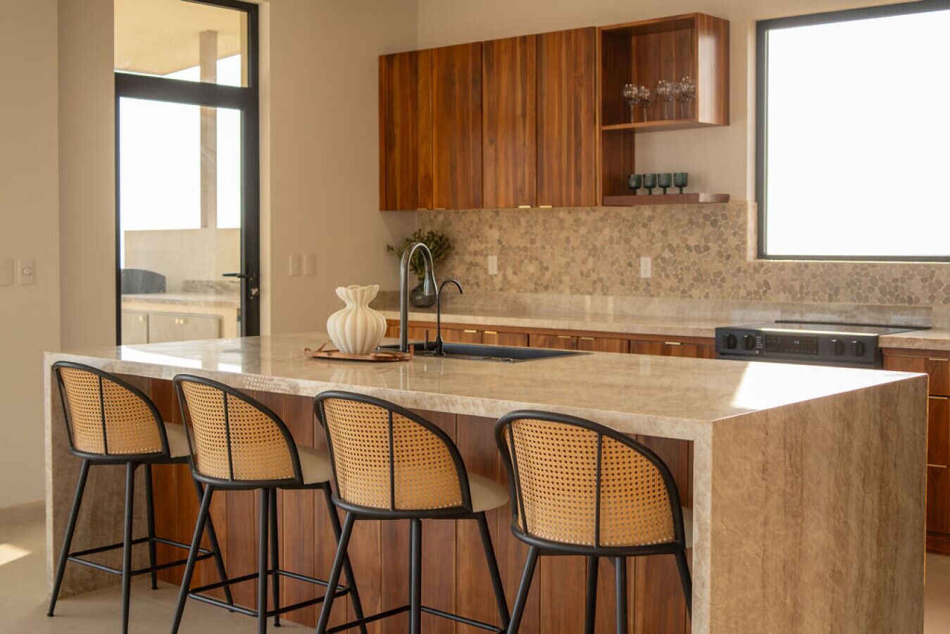 A kitchen with a large island, bar stools, wooden cabinets, and a stone backsplash.