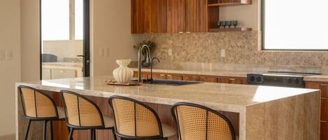 A kitchen with a large island, bar stools, wooden cabinets, and a stone backsplash.